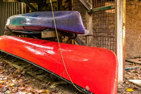 Brightly colored canoe & kayak, stored near cut wood, autumn leaves falling.