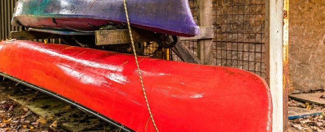 Brightly colored canoe & kayak, stored near cut wood, autumn leaves falling.